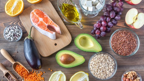 Verschiedene Lebensmittel, die wenig bis kein Cholesterin enthalten liegen auf einem Holztisch.