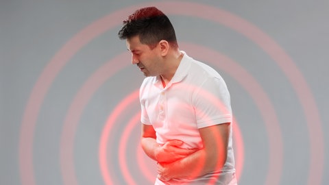 Ein junger Mann hält sich mit beiden Armen den Bauch. Es scheint, er hat Probleme in der Bauchregion. Heftige Bauchschmerzen und Durchfall können Symptome für chronisch-entzündliche Darmerkrankungen sein. Es gibt diverse Therapiemöglichkeiten.