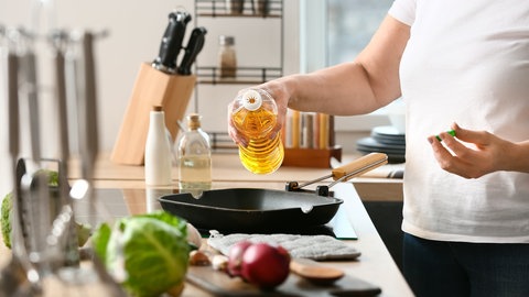 Person gießt Öl aus einer Plastikflasche in eine Bratpfanne. Welches Fett eignet sich zum Braten?