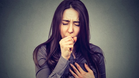 Frau hustet in die Faust, macht ein angestrengtes Gesicht und hält sich die Brust. Ist das Husten oder schon Asthma? Was bringt die Antikörper-Therapie?