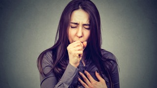 Frau hustet in die Faust, macht ein angestrengtes Gesicht und hält sich die Brust. Ist das Husten oder schon Asthma? Was bringt die Antikörper-Therapie?