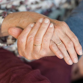 Hände von zwei Menschen, die sich halten. Kribbeln, Taubheit, brennende Füße – können auf eine Polyneuropathie hinweisen. Millionen sind betroffen, oft durch Diabetes oder nach einer Chemotherapie. Vielen hilft Bewegung.