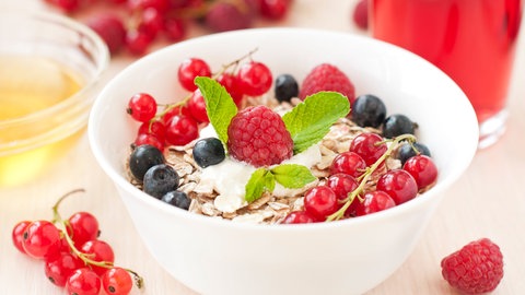 Haferflocken und frisches Obst in einer Müslischale: Hafer etwa zum Frühstück macht lange satt und ist sehr gesund.