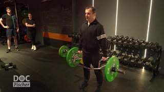 Männliche Person beim Krafttraining, zwei Personen sehen zu