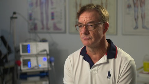 Sportmediziner Dr. Jens Stening, hinter ihm sind medizinische Geräte und Bilder an der Wand zu sehen.