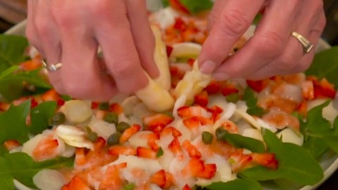 Man sieht die Hände von Dagmar von Cramm, Ernährungswissenschaftlerin, die ein Spargelcarpaccio auf Babyspinat und Löwenzahn mit Erdbeer-Kapern-Vinagraitte zubereiten.