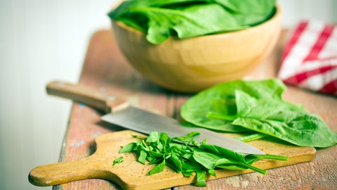 Spinat liegt geschnitten auf einem Brett. Spinat ist gesund und lecker. Mit welchen Rezepten schmeckt das Blattgemüse am besten? Und hilft Spinat möglicherweise beim Muskelaufbau? 