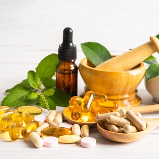Zu sehen sin verschiedene Formen von Vitamin E Nahrungsergänzungsmitteln: Gelbe Pillen und Tropfen in einerm braunen Fläschchen. Es schützt Zellen vor oxidativem Stress und ist wichtig für das Immunsystem – Vitamin E. Wir zeigen neue Erkenntnisse dazu und zu Nahrungsergänzungsmitteln. 