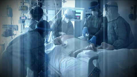 In einem Operations-Saal stehen Ärzte und Assistenten um einen Patienten, der mit dem Bauch auf einer Liege liegt.