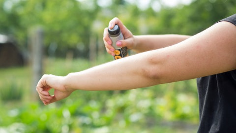 Frau sprüht ihren Arm mit Insektenschutzmittel ein.