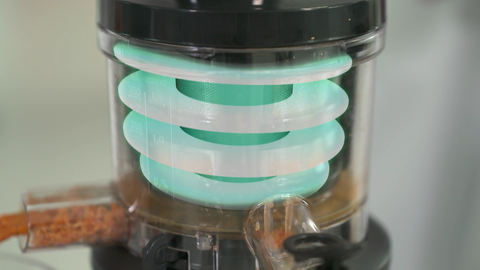 „Slow-Juicer” bedeutet zu Deutsch „langsamer Entsafter”, da er das Obst und Gemüse mit langsamer Geschwindigkeit zerkleinert. Nahaufnahme von einem Slow-Juicer beim Auspressen von Karrotten.