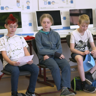 Drei Kinder sitzen in einem Klassenzimmer und bereiten eine Debatte vor.