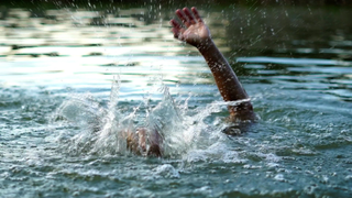 Eine Person kämpft dagegen an, im Wasser unterzugehen. Ihr Arm ragt aus dem Wasser heraus.