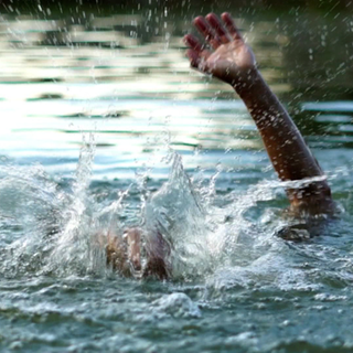 Eine Person kämpft dagegen an, im Wasser unterzugehen. Ihr Arm ragt aus dem Wasser heraus.