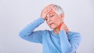 Frau hält sich die Stirn und den Nacken, sie hat Kopfschmerzen
