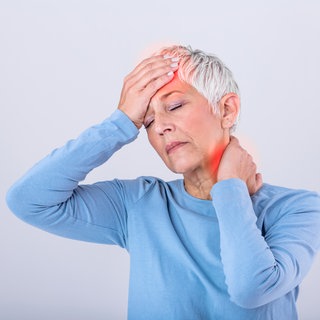 Frau hält sich die Stirn und den Nacken, sie hat Kopfschmerzen