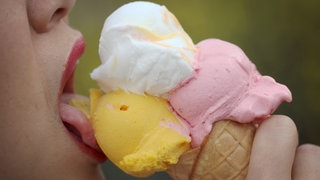 Eine Frau bein Eis essen. Sie leckt Eiscreme in einer Eiswaffel mit drei Kugeln.