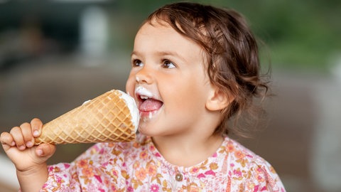 Ein glückliches Kind beim Eis essen. Es leckt Eiscreme in einer Eiswaffel.