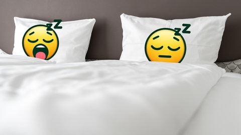 Ein Bett mit zwei weißen Decken und zwei weißen Kissen mit zwei schlafenden Emojigesichern.