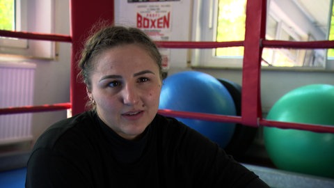 Boxerin Melina Maibaum sitzt vor dem Boxring. Im Hintergrund ist ein blauer Gymnastikball zu sehen.