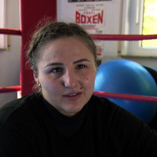 Boxerin Melina Maibaum sitzt vor dem Boxring. Im Hintergrund ist ein blauer Gymnastikball zu sehen.