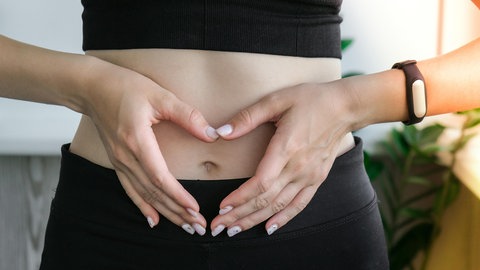 Eine Frau hält die Hände zum Herz geformt über ihren Bauch | Mikrobiom und Darmgesundheit: Das könnt ihr für einen gesunden Darm tun