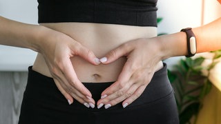 Eine Frau hält die Hände zum Herz geformt über ihren Bauch | Mikrobiom und Darmgesundheit: Das könnt ihr für einen gesunden Darm tun