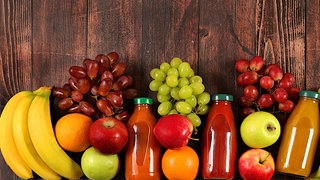 Bananen, Äpfel und Weintrauben liegen mit Fruchtsäften auf einem Holztisch | Gesund leben mit den richtigen Vitaminen: Die Vitamine von A bis E im Überblick