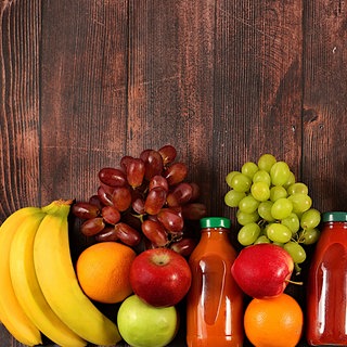 Bananen, Äpfel und Weintrauben liegen mit Fruchtsäften auf einem Holztisch | Gesund leben mit den richtigen Vitaminen: Die Vitamine von A bis E im Überblick