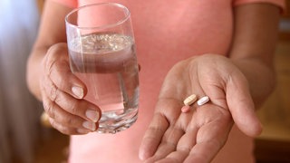 Eine Frau hält Tabletten und ein Glas Wasser in den Händen | Neurologin Prof. Dr. Ulrike Bingel zu Placebo- und Noceboeffekt