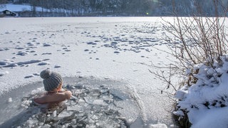 Eine Frau beim Eisbaden im Lauser Weiher bei einer gefrorenen Wasserfläche im Winter. | Schwimmen in extremer Kälte: Wie gesund ist Eisbaden wirklich?