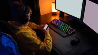 Internetsucht bei Kindern - eine Expertin verrät, was Eltern tun können. Es geht um Sicherheit und Schutz im Cyberspace - wie wehre ich mich gegen Hacker, Betrüger und Spammer, gegen Scammer, Idenditätsdiebstahl und Pädophile? Wir zeigen Euch, wie Ihr Euch und Eure Kinder vor Gefahren im Internet schützen könnt - nicht nur am Safer Internet Day! Das Symbolbild zeigt ein Kind, das mit einem Handy vor einer Computertastatur und einem Bildschirm sitzt.