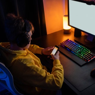 Internetsucht bei Kindern - eine Expertin verrät, was Eltern tun können. Es geht um Sicherheit und Schutz im Cyberspace - wie wehre ich mich gegen Hacker, Betrüger und Spammer, gegen Scammer, Idenditätsdiebstahl und Pädophile? Wir zeigen Euch, wie Ihr Euch und Eure Kinder vor Gefahren im Internet schützen könnt - nicht nur am Safer Internet Day! Das Symbolbild zeigt ein Kind, das mit einem Handy vor einer Computertastatur und einem Bildschirm sitzt.