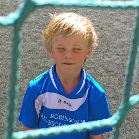 Ein kleiner, blonder Junge in blauem Fußball-Trikot schaut durch ein Tornetz. Ein junger Mann spielt im weißen Trikot Fußball. SWR1 Neuanfang: Nachwuchsfußballer Max und sein Kampf gegen den Krebs. Bei dem jungen Mann aus Heidelberg wird ein Sarkon diagnostiziert, ein höchst aggressiver Krebs. Der Sport und seine Familie geben ihm die Kraft, die Chemotherapie und den Kampf gegen den Krebs erfolgreich zu bestehen.