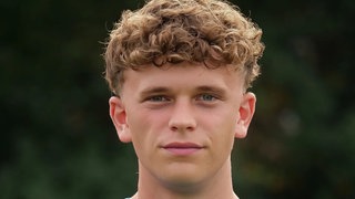 Ein junger Mann mit braunen Locken und blauem Trikot. SWR1 Neuanfang: Nachwuchsfußballer Max und sein Kampf gegen den Krebs. Bei dem jungen Mann aus Heidelberg wird ein Sarkon diagnostiziert, ein höchst aggressiver Krebs. Der Sport und seine Familie geben ihm die Kraft, die Chemotherapie und den Kampf gegen den Krebs erfolgreich zu bestehen.