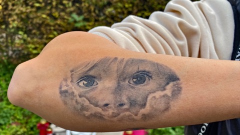 Eine Tatöwierung auf einem Unterarm: sie zeigt das Gesicht eines kleinen Kindes, das mit großen, dunklen Augen durch ein Loch in den Wolken schaut. In unserer Reihe "SWR1 Neuanfang" portraitieren wir Luana: Sie hat einen Raserunfall überlebt, ihr Mann und ihr Baby starben. Trotz des großen Traumas kämpfte sie sich zurück ins Leben.