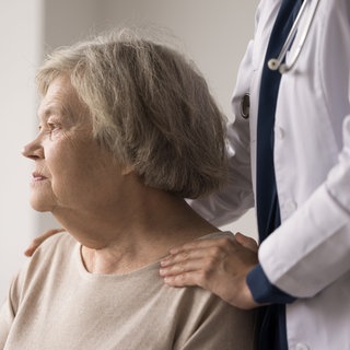 Arzt legt älterer Frau Hände auf die Schultern