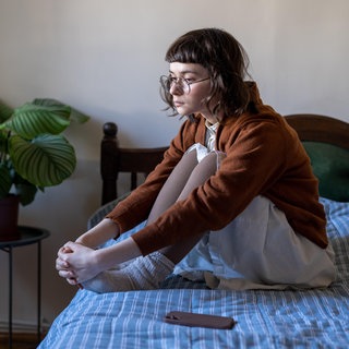 Eine Frau sitzt traurig mit den Knien angewinkelt alleine auf dem Bett | Einsamkeit und mentale Gesundheit: Warum Stress uns einsam macht