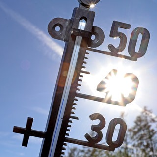 Ein Thermometer vor blauem Himmel und der Sonne 