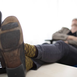 Mann schläft mit Füßen auf dem Schreibtisch. Wer auf der Arbeit einen Mittagsschlaf macht, könnte produktiver werden. Denn der Powernap verhilft zu Geistesblitzen.