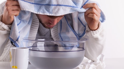 Ein Mann inhaliert über einer dampfenden Schüssel. Eine Erkältungswelle, wie sie aktuell vom RKI in Deutschland verzeichnet wird, ist im Herbst typisch.