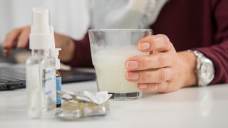 Eine Person nimmt Aspirin, daneben Taschentücher und Nasenspray. In Deutschland ist aktuell jeder Elfte krank.
