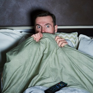 Mann schaut im Bett fernsehen und gruselt sich