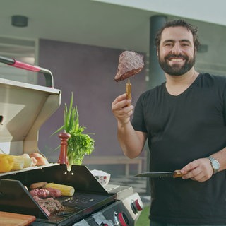 Mann steht am Grill und hält Steak mit Gabel