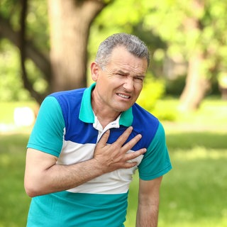 Ein älterer Mann greift sich mit schmerzverzerrtem Gesicht an den Brustkorb im Bereich des Herzens. Das kann ein Symptom für eine Aortenaneurysma - erweiterte Hauptschlagader - sein.