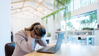 Frau sitzt am Laptop und greift sich in den Nacken 