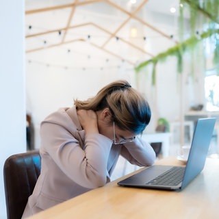 Frau sitzt am Laptop und greift sich in den Nacken 