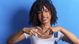 Ein Mädchen formt mit ihren Händen ein Herz und lächelt freundlich | Darum ist Freundlichkeit gut für unsere Gesundheit