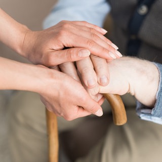 Junge Pflegekraft hält älterem Mann die Hände