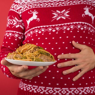 Mann mit Weihnachtspulli hat zu viel gegessen